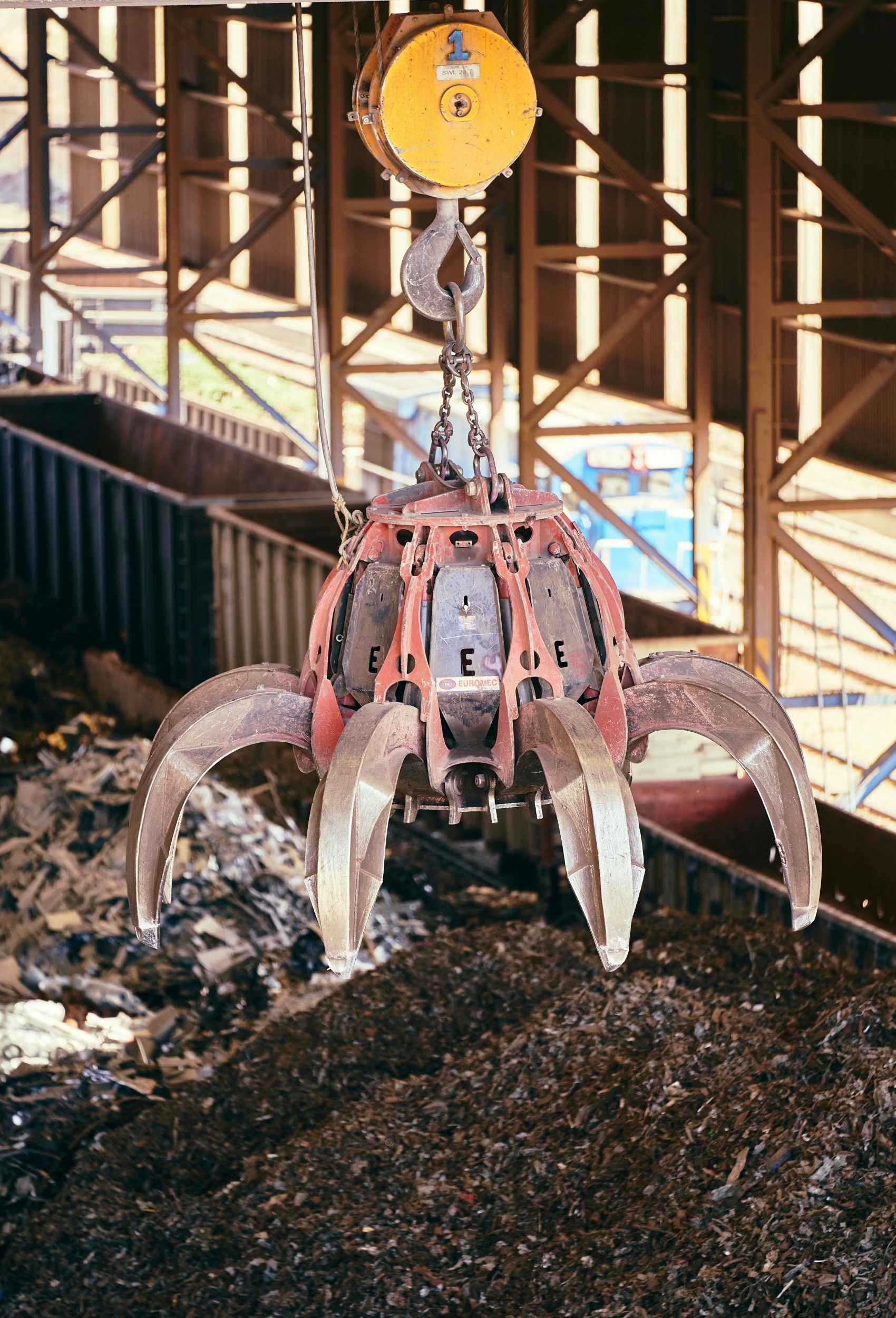 Close-up of a claw crane grasping scrap metal at a recycling plant.